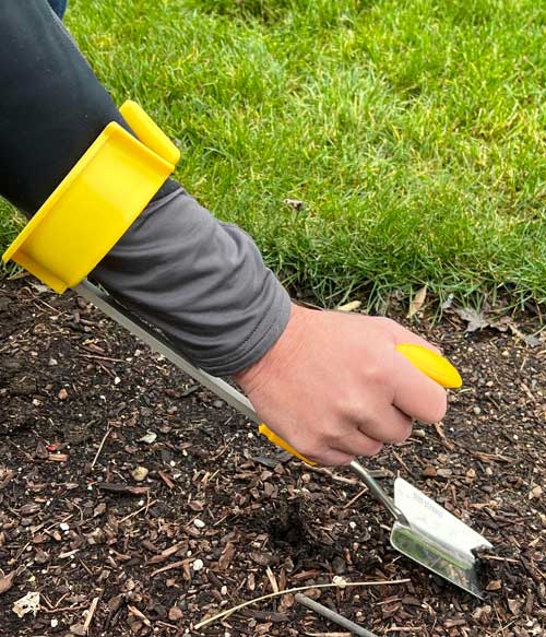 a person using a hand weeder tool that wraps around the forearm to assist